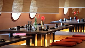 A restaurant with long tables, red cushions, and a bottle of sake.