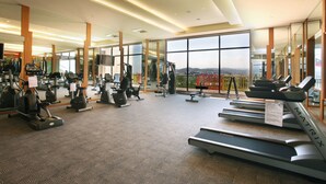A spacious gym with treadmills, ellipticals, and weight machines. Large windows offer a view of the city.
