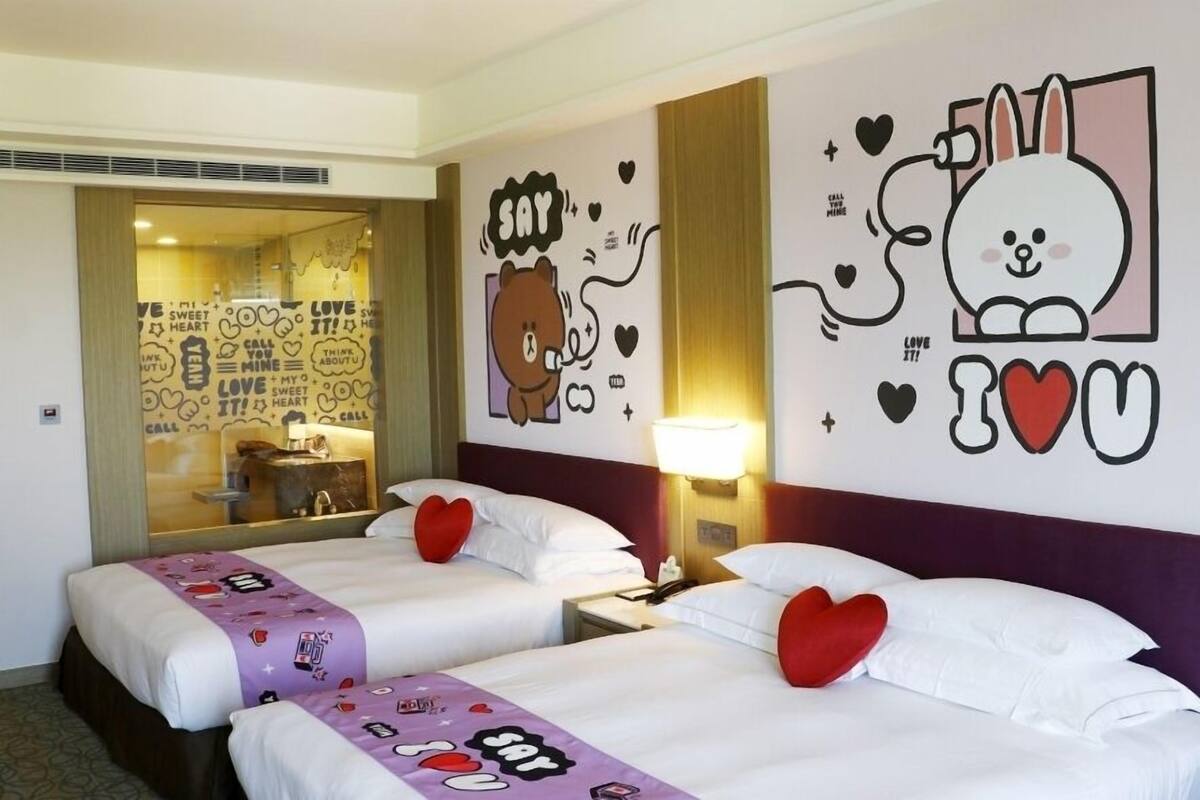 Een hotelkamer met twee bedden, een spiegel, een muur met decoratieve tekeningen en een raam met uitzicht.