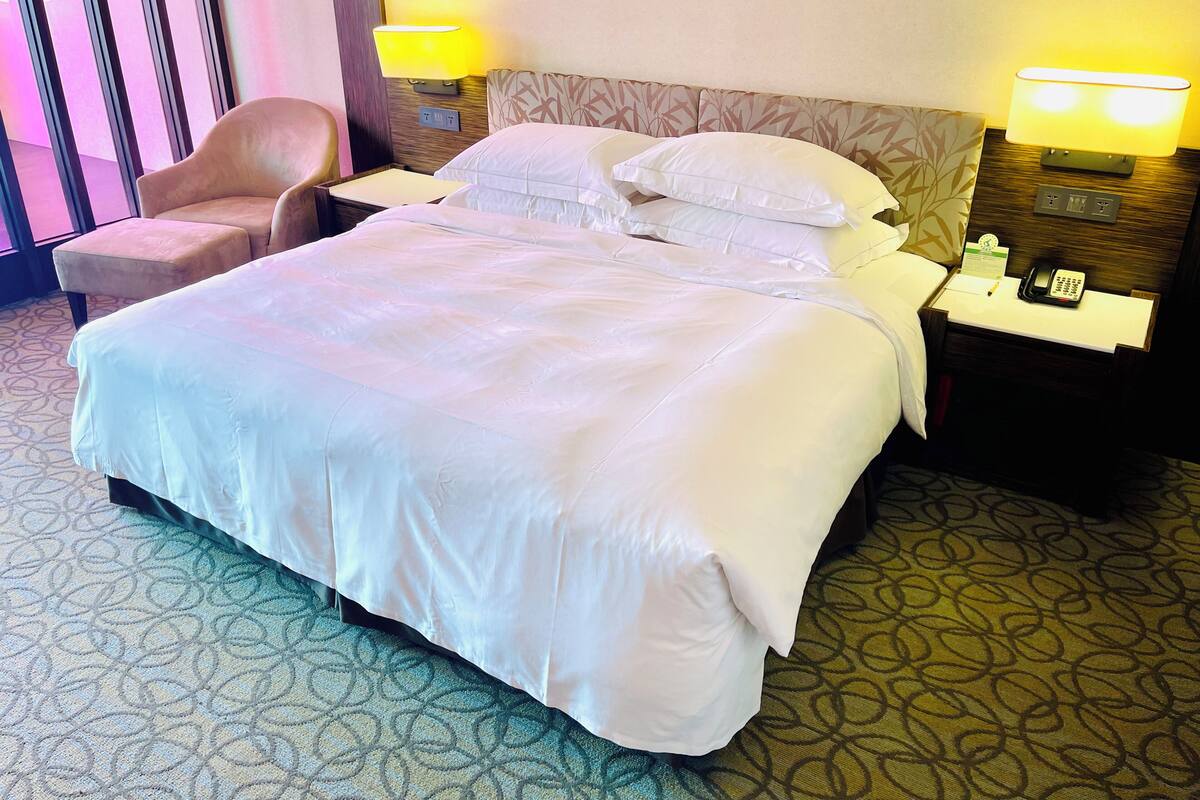Ein Hotelzimmer mit einem großen Bett, zwei Nachttischlampen, einem Sessel, einem Telefon am Nachttisch und einem Teppichboden.