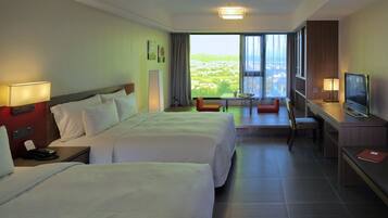 Ein Hotelzimmer mit zwei Betten, einem Schreibtisch, einem Fernseher und Blick auf eine Stadtlandschaft.