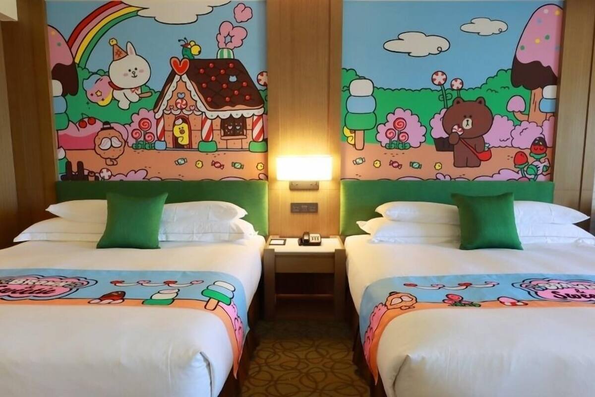 Ein Hotelzimmer mit zwei Betten, jedes mit einem grünen Kopfkissen und einer Bettdecke mit Comic-Motiven.