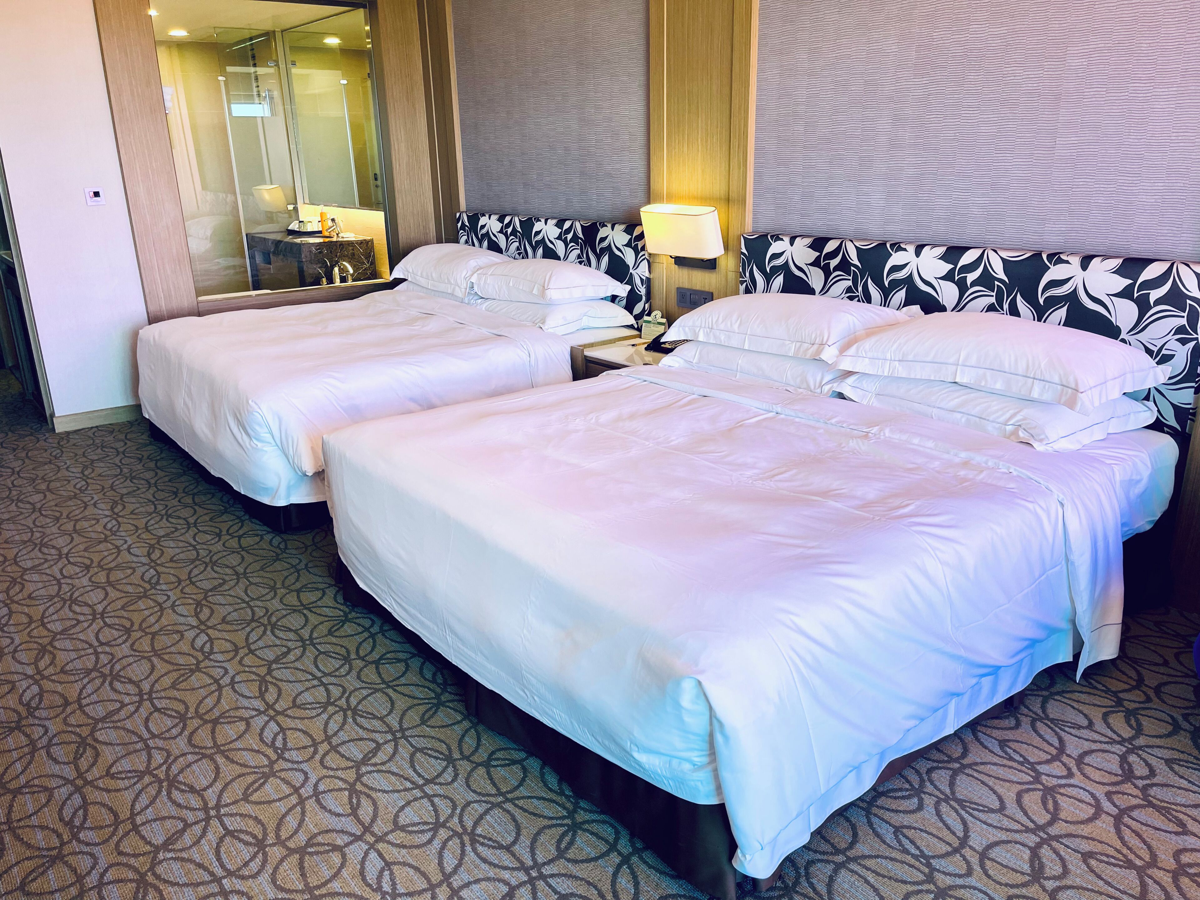 Una habitación de hotel con dos camas, un espejo, una mesita de noche y una alfombra estampada.