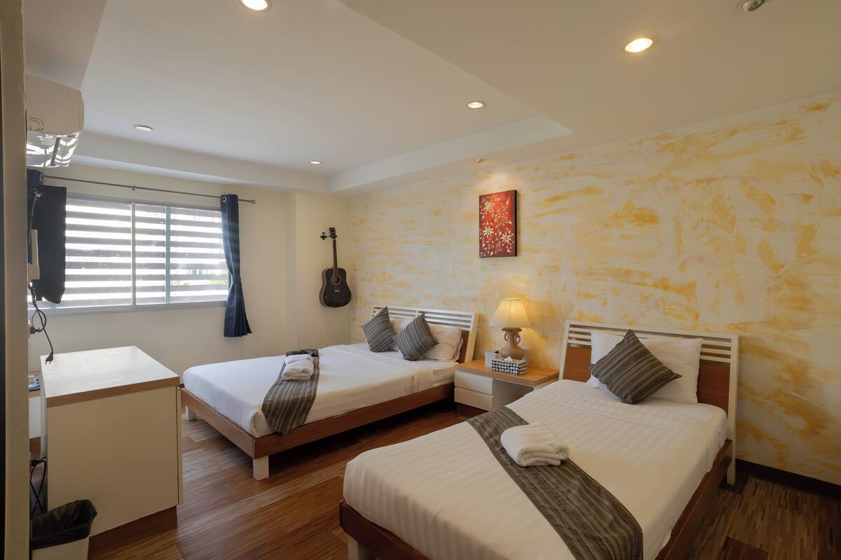 A hotel room with two single beds, a desk, a guitar, and a lamp.