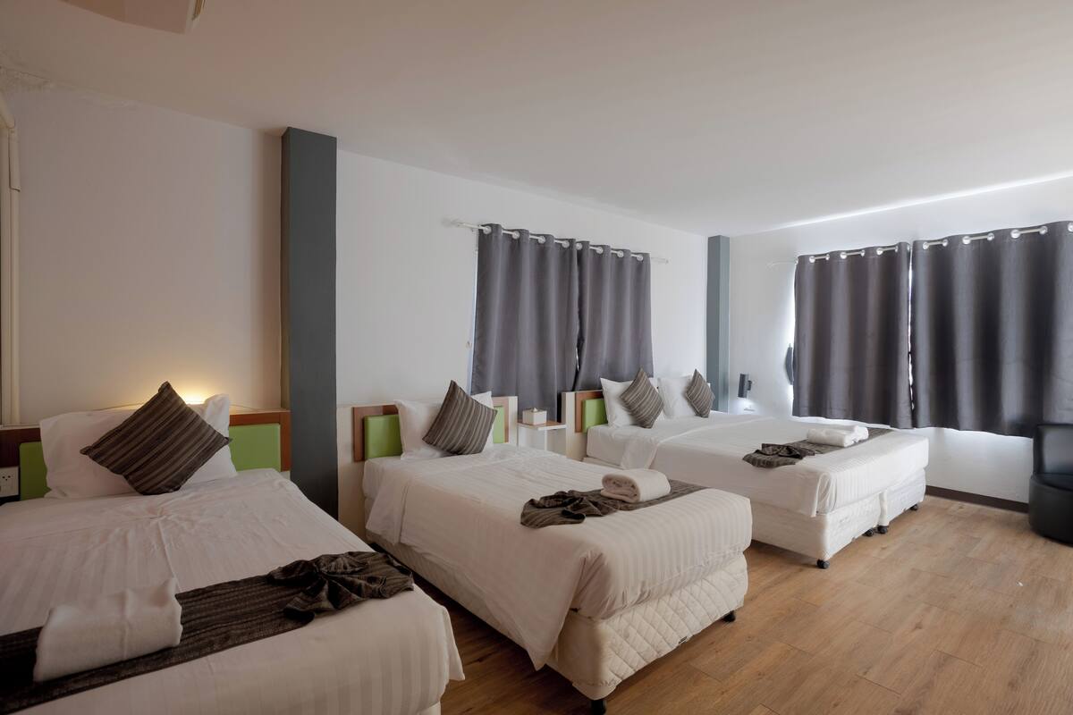 A hotel room with three beds, each with a pillow and a blanket.