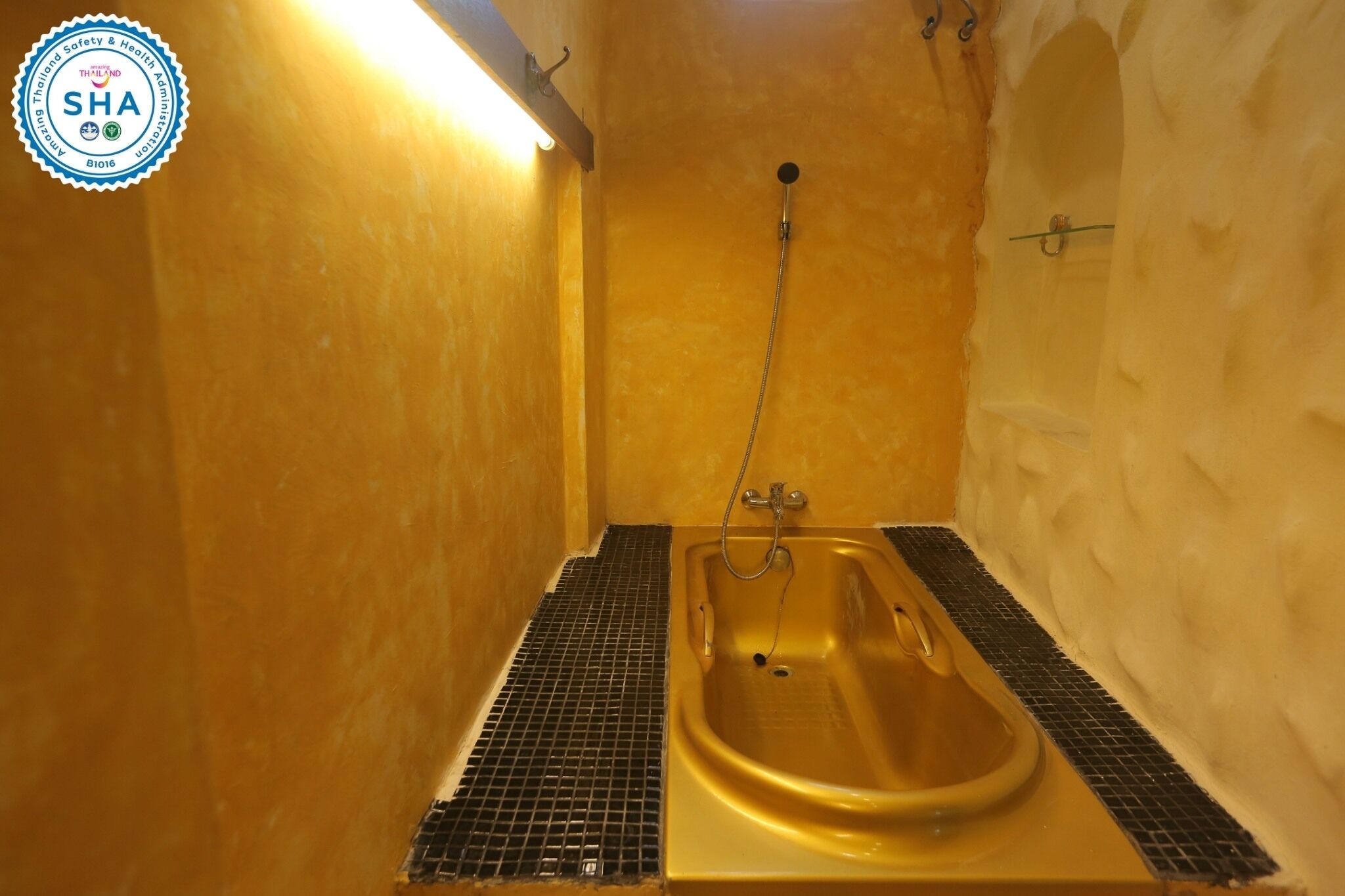 A small, enclosed bathroom with a gold bathtub, a showerhead, and a tiled floor.