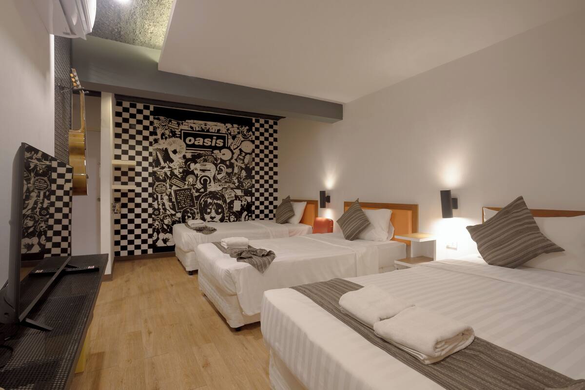 A hotel room with two beds, a checkered wall mural, a treadmill, and a television.