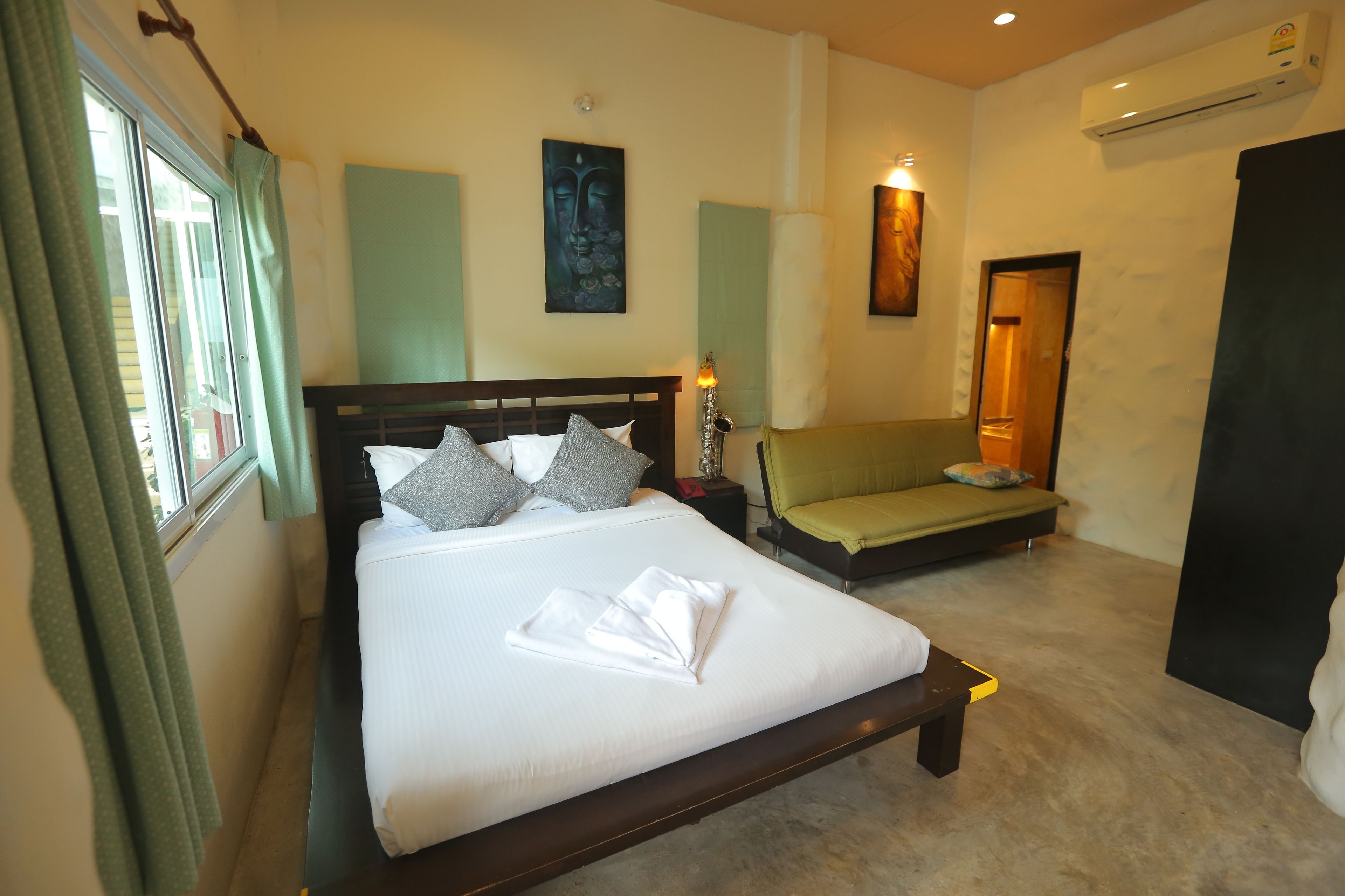 A hotel room with a bed, bedside table, lamp, and a green sofa.