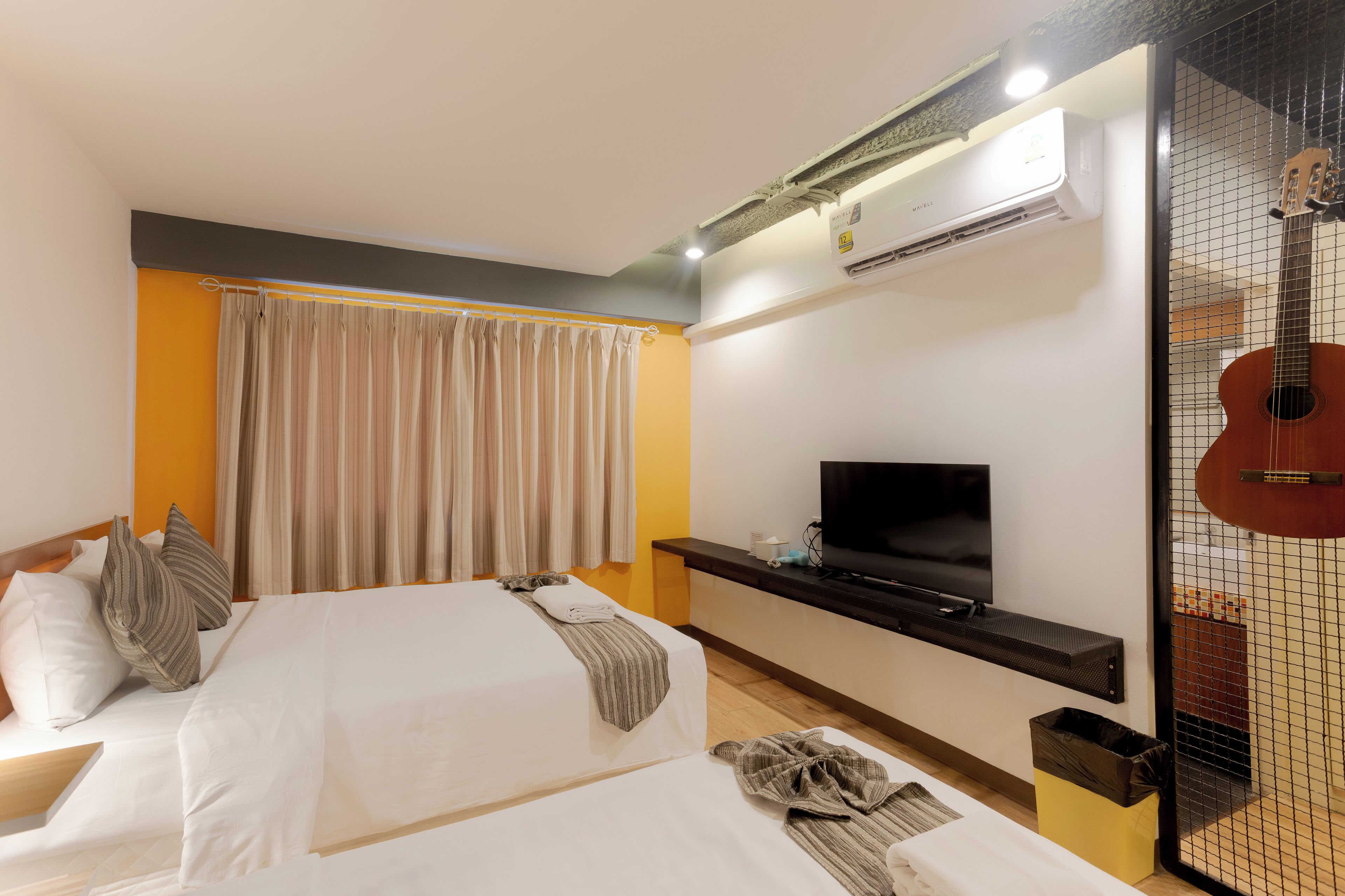 A hotel room with two beds, a TV, an air conditioner, and a guitar.