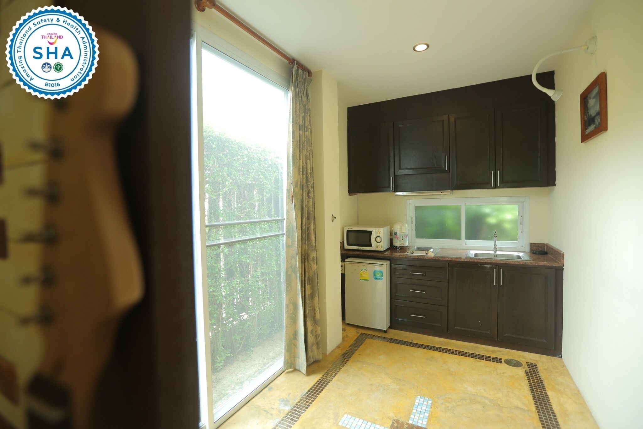 A kitchen with dark cabinets, a microwave, a refrigerator, and a window with curtains.
