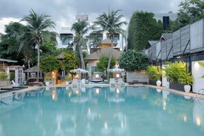 A swimming pool with lounge chairs and umbrellas, surrounded by palm trees and a building with a sloped roof. - My Way Hua Hin Music Hotel (Hua Hin)