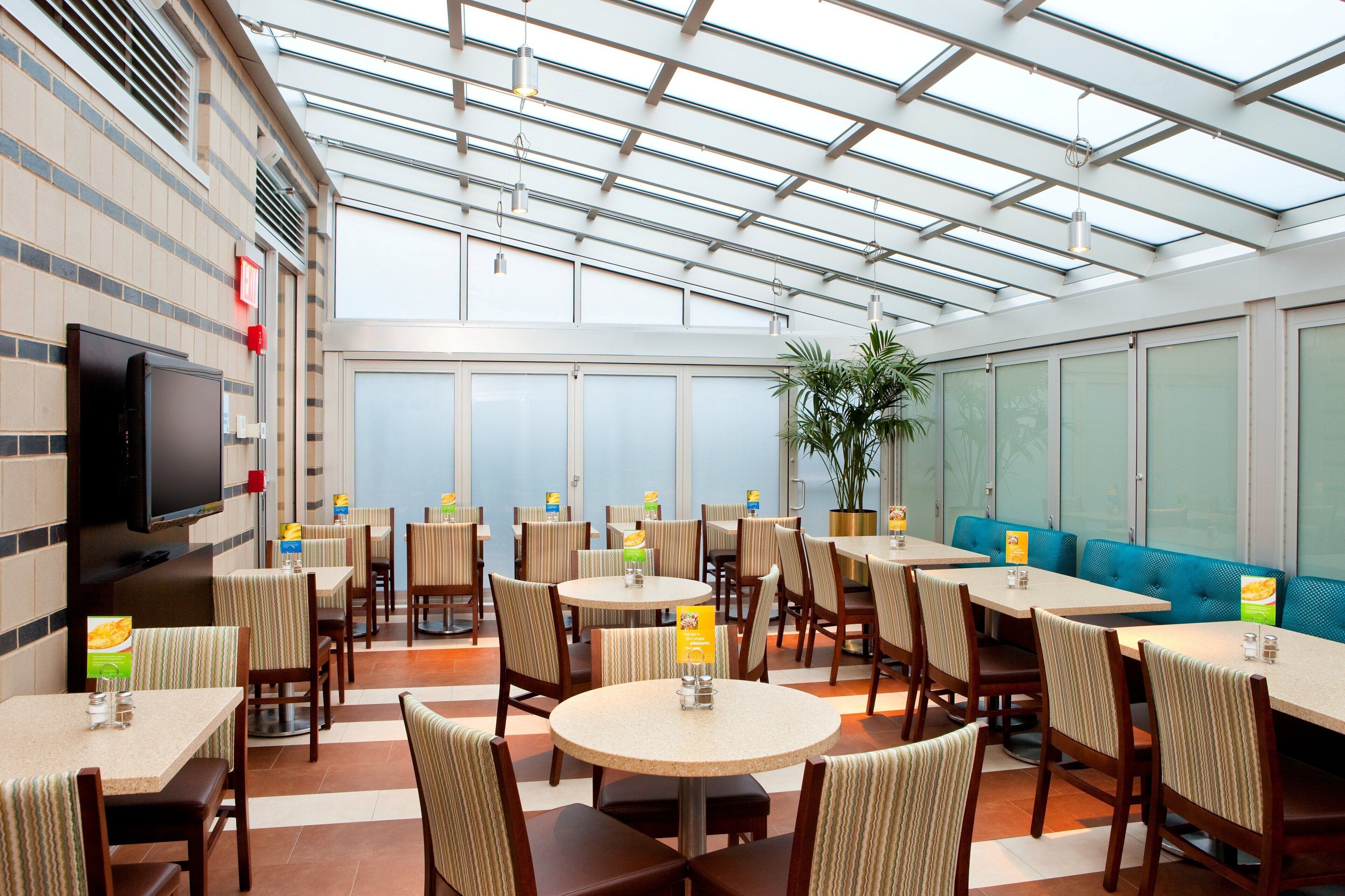 A restaurant with high ceilings, a glass roof, and multiple seating areas including round tables and booths.