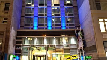 A multi-story hotel with a prominent entrance, large windows, and a 'NOW OPEN' sign.