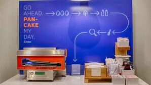 Un coin petit-déjeuner avec un téléviseur à écran plat affichant un menu de petit-déjeuner, une machine à café et divers articles pour le petit-déjeuner disposés sur le comptoir.