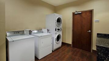 A laundry area with two washing machines and a dryer, a wooden door, and a storage sign.