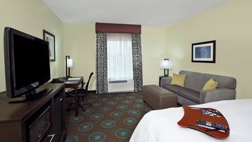 Een hotelkamer met een flatscreen-tv, een bureau met een lamp, een sofa en een bed.