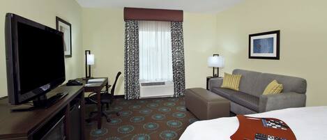 A hotel room with a flat-screen TV, a desk with a lamp, a sofa, and a bed.