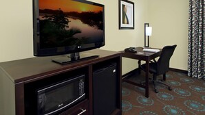 A hotel room with a flat-screen TV, a desk with a chair, a microwave, and a refrigerator.