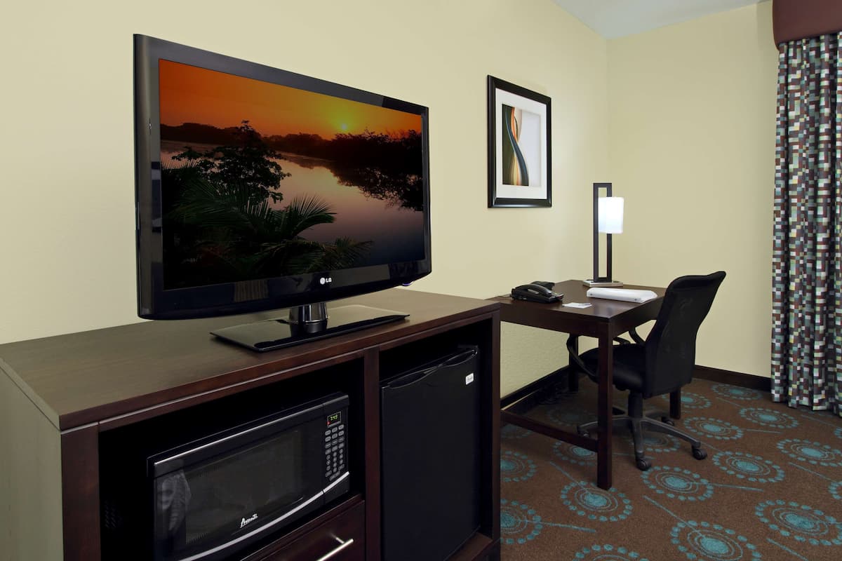Ett hotellrum med en platt-TV, ett skrivbord med en stol, en mikrovågsugn och ett kylskåp.