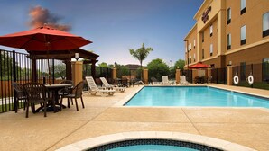 A hotel pool area with lounge chairs, umbrellas, and a tiled pool edge.