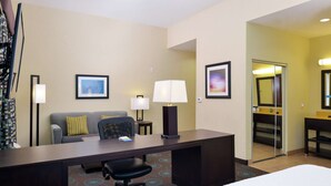 A hotel room with a bed, a desk with a chair, a sofa with pillows, a lamp, and a framed picture on the wall.