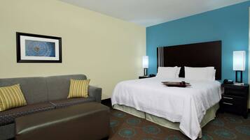 A hotel room with a bed, a sofa, a nightstand, and a framed picture on the wall.