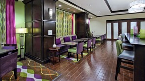 A hotel lobby with a seating area, a reception desk, and a dining area.