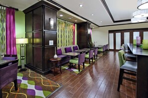 A hotel lobby with a seating area, a reception desk, and a dining area.