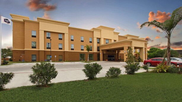 A multi-story hotel with a flat roof, a central entrance, and a parking lot.