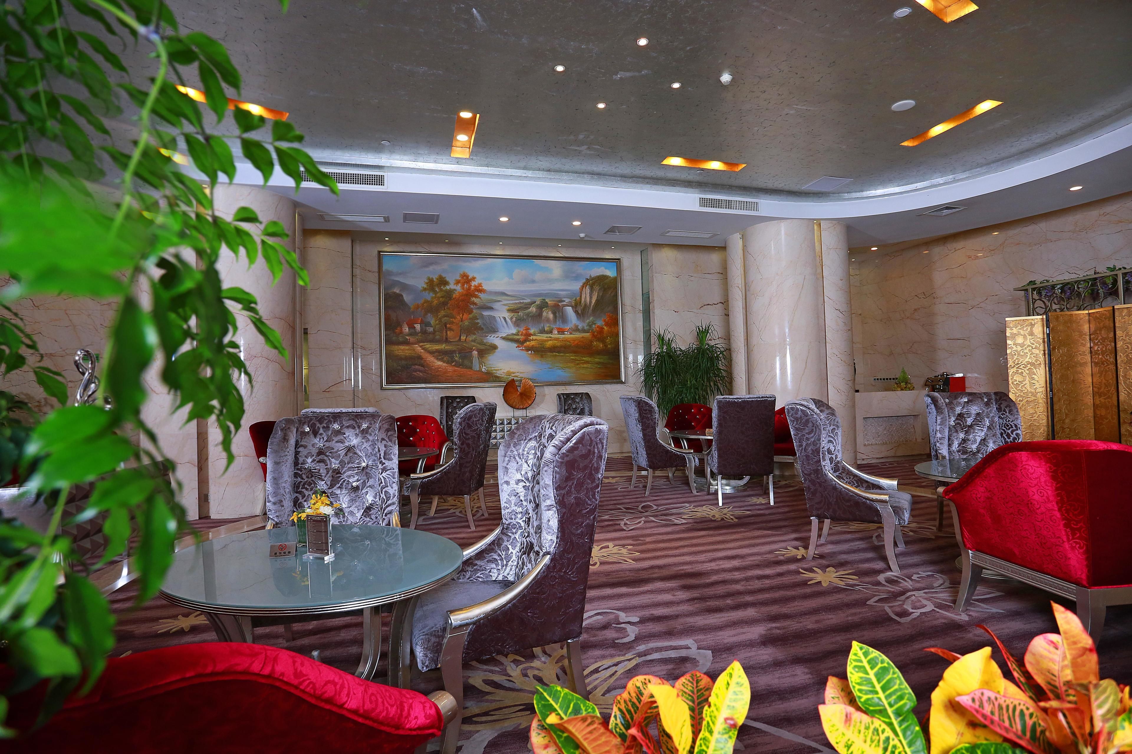 En hotellobby med et stort muralmaleri, runde borde og moderne stole.