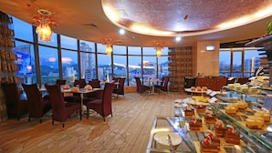 A restaurant with a panoramic city view, large windows, and a variety of desserts displayed on a glass counter.