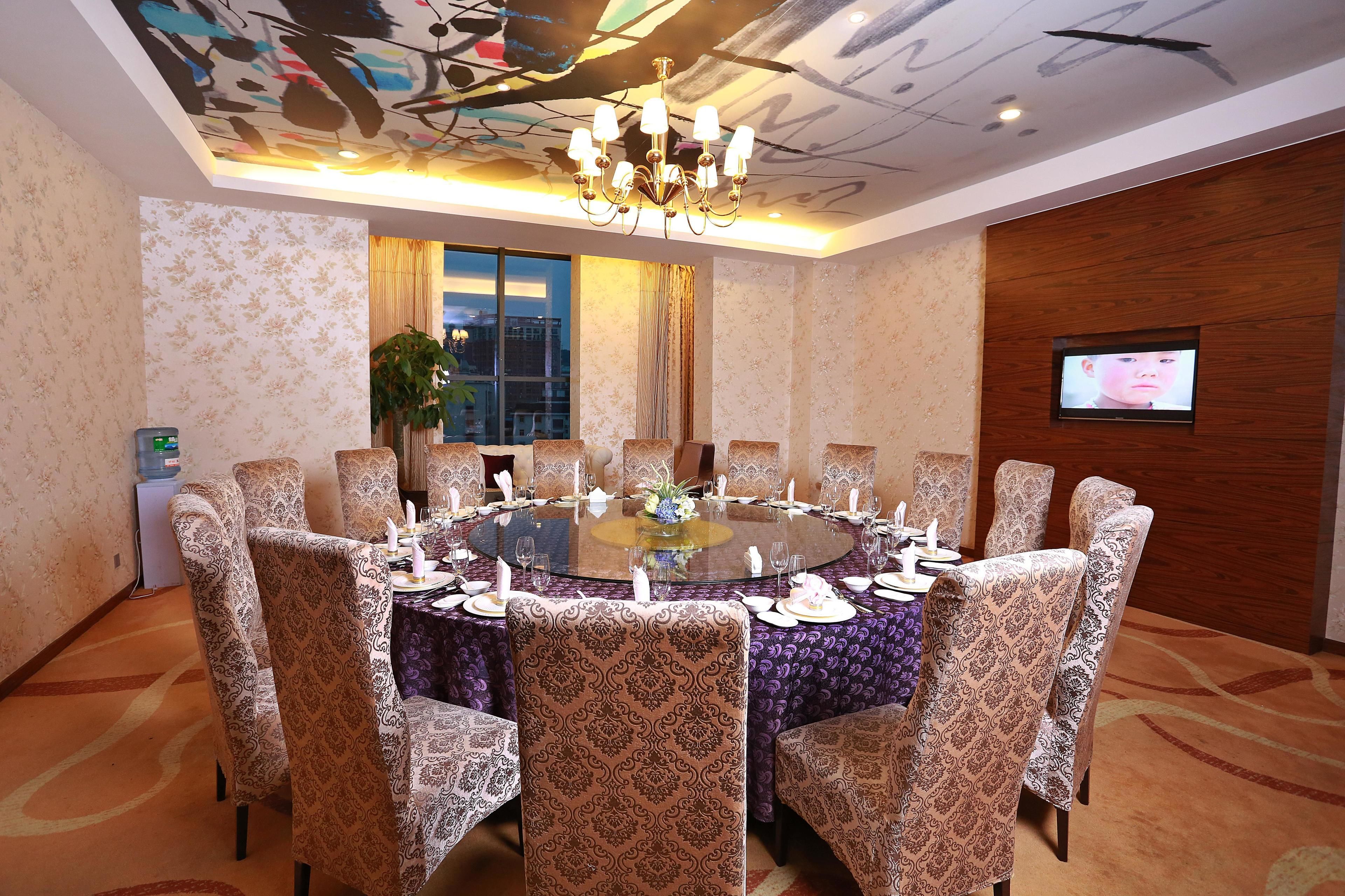 A conference room with a round table, patterned chairs, a chandelier, a television, and a window with a view.