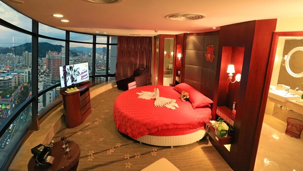 A modern hotel room with a large bed, a TV, a city view, and a balcony.