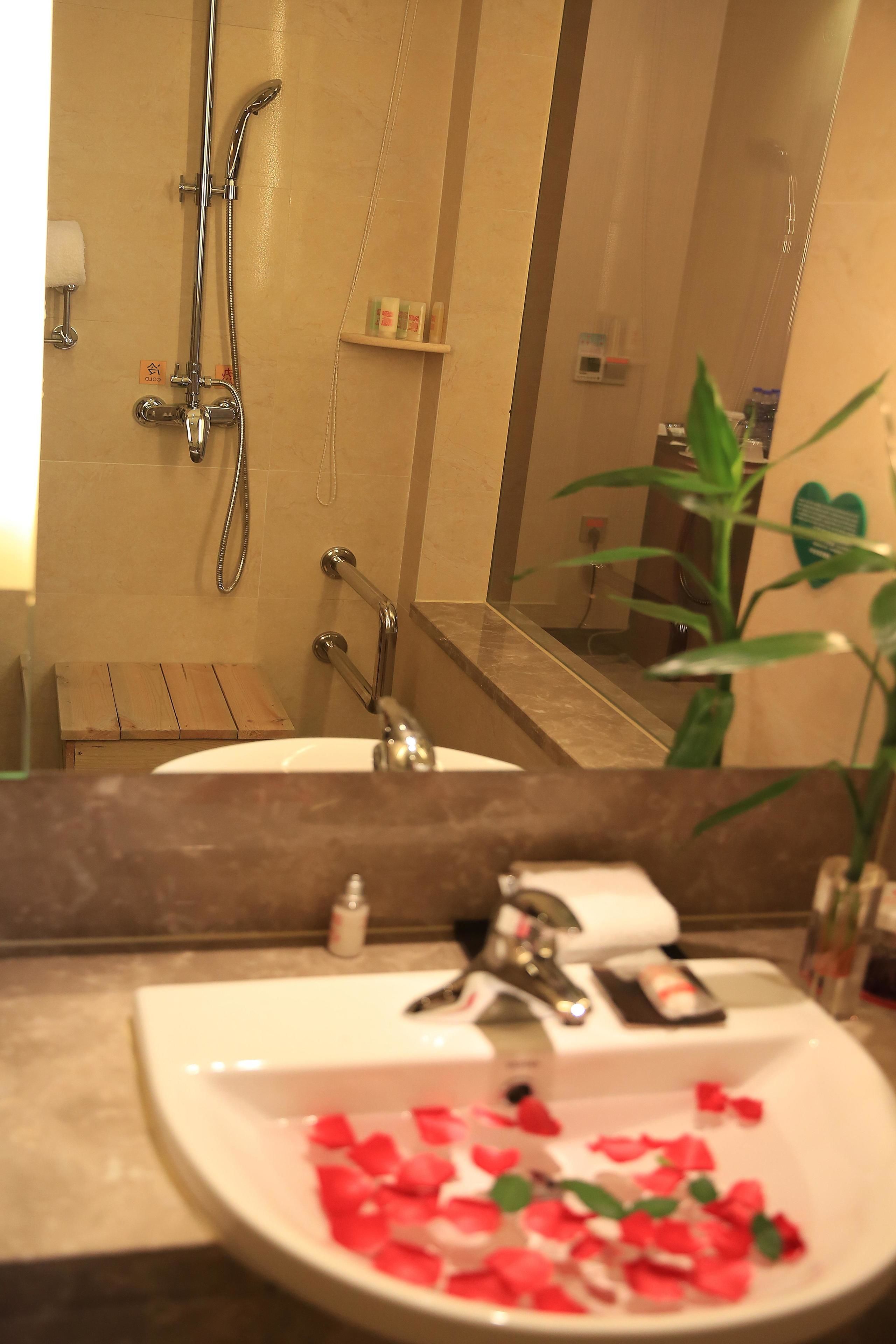 A bathroom with a shower, a sink with rose petals, and a mirror.