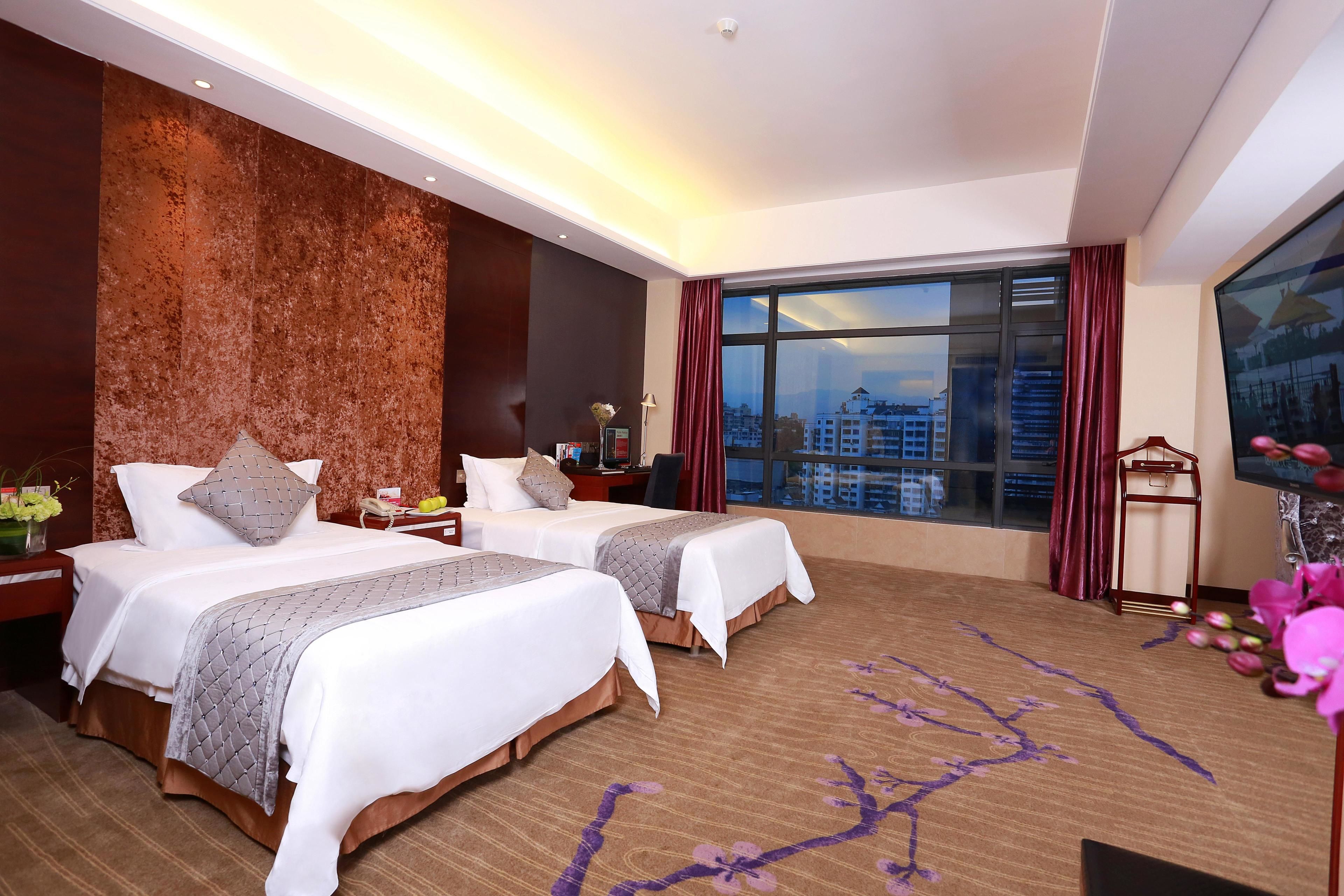 Ein Hotelzimmer mit zwei Betten, einem großen Fenster mit Blick auf die Stadt, einer Wand mit Holzverkleidung und einem Flachbildfernseher.