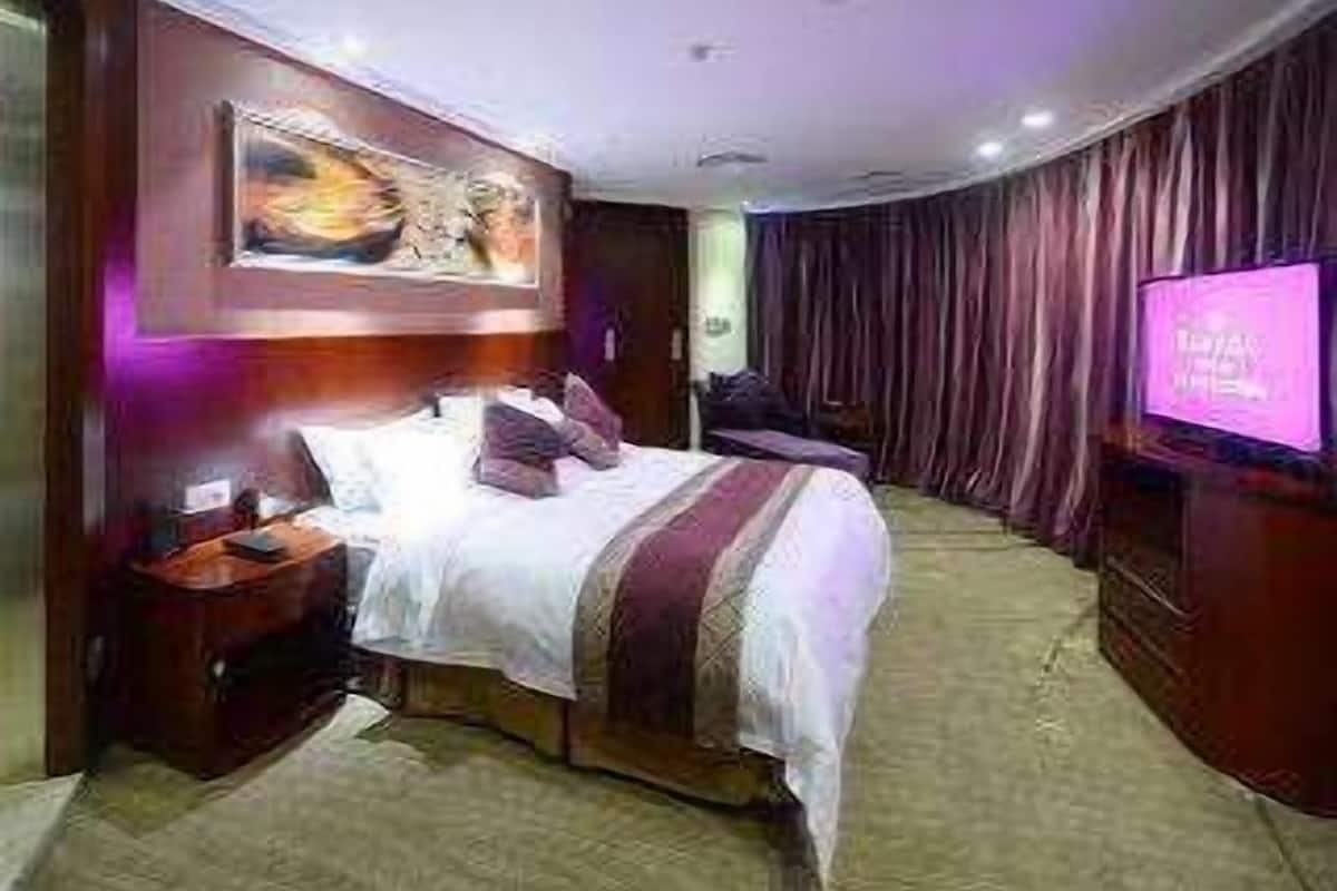 A hotel room with a large bed, a TV on the wall, and a curtain-covered window.
