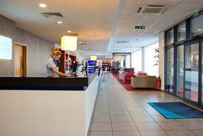En hotellobby med en receptionsdisk, en tv-skärm och en sittgrupp med stolar och en soffa.