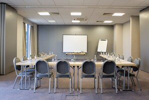Ett konferensrum med ett långt bord, stolar, en whiteboard och en blädderplanshållare.