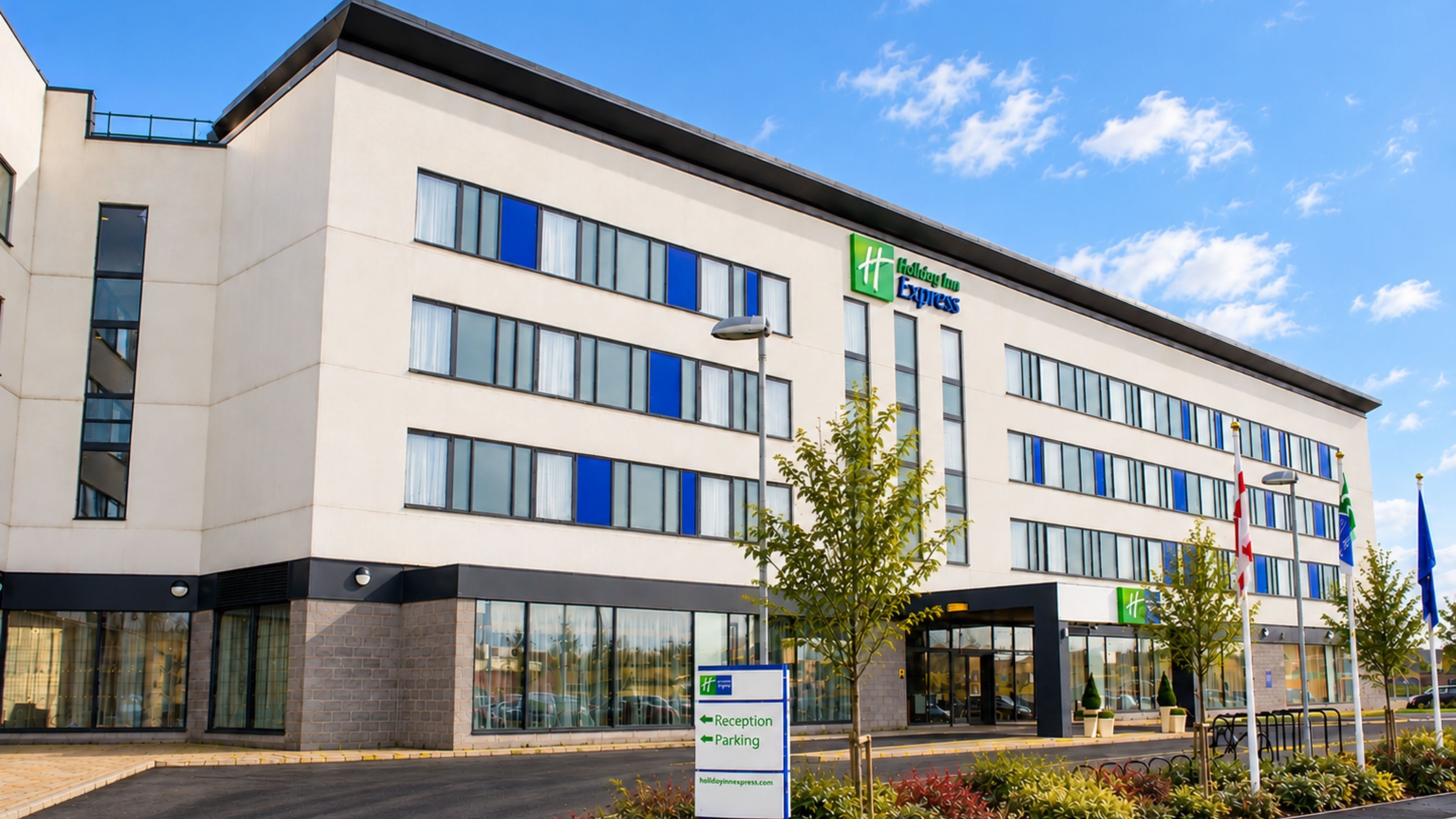 A modern hotel building with a reception desk, parking sign, and multiple windows.