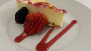 Uma fatia de cheesecake com morangos e uma framboesa em um prato branco.