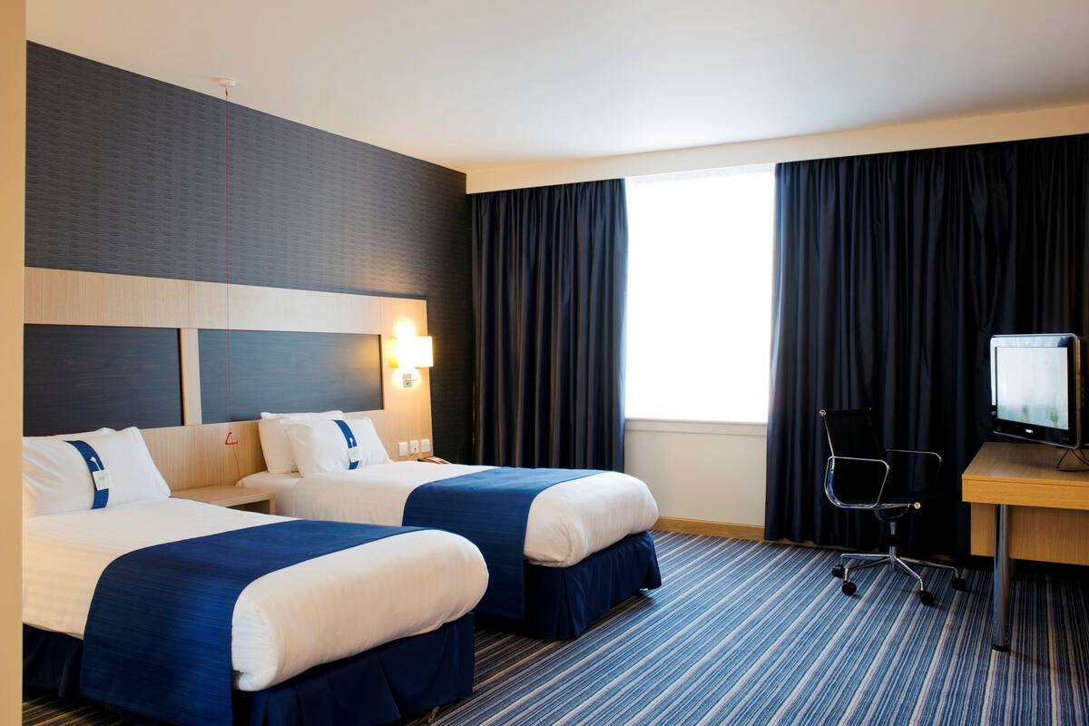 A hotel room with two beds, a desk, a chair, and a television.