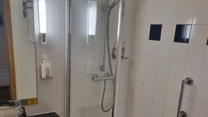 Casa de banho com chuveiro em cabine de vidro, lavatório preto e parede revestida a mosaico branco.