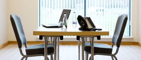 A conference room with a table, two chairs, a laptop, a bottle, and a telephone.