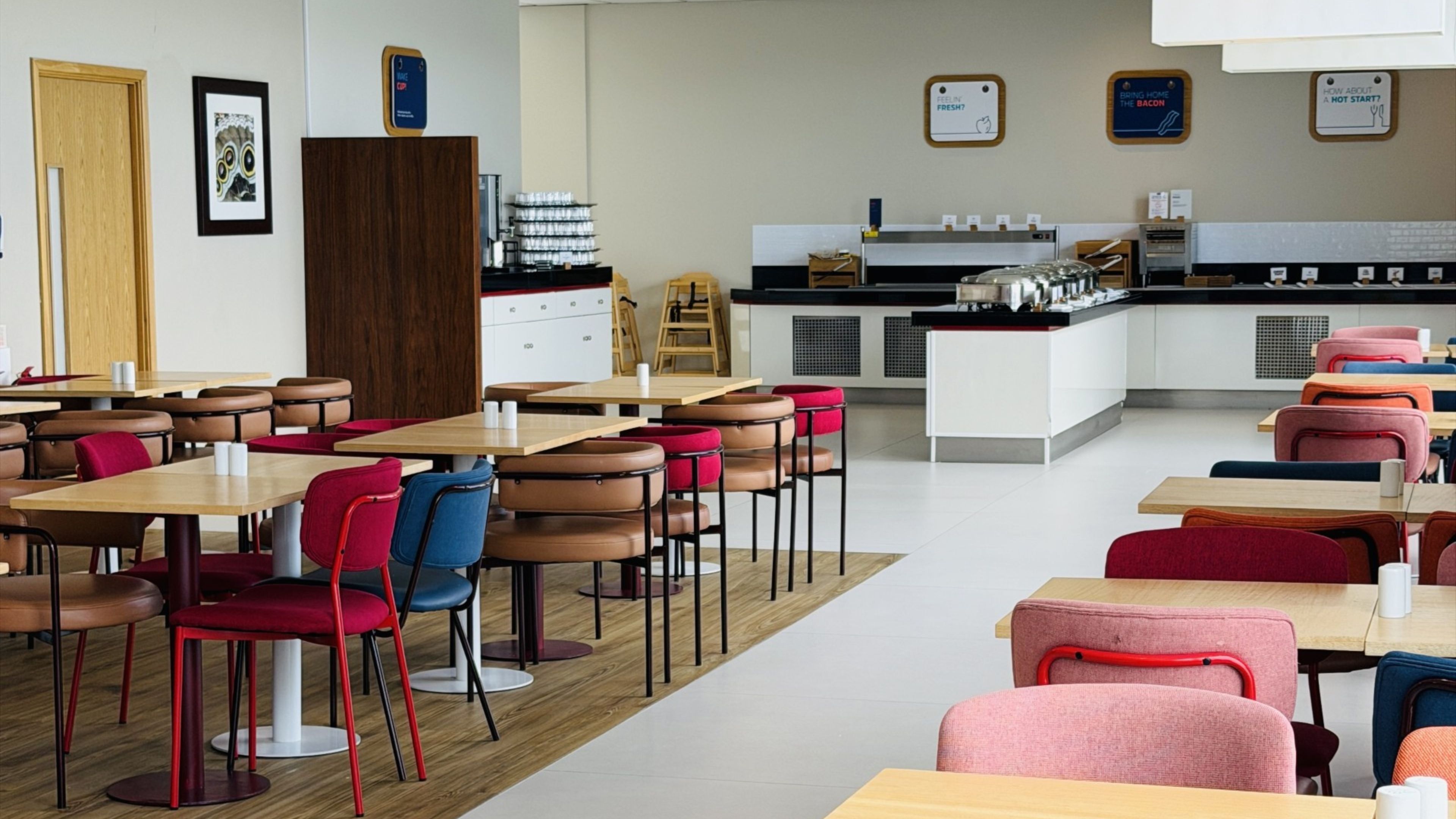 A modern dining area with multiple tables and chairs, a kitchen in the background, and a framed picture on the wall.