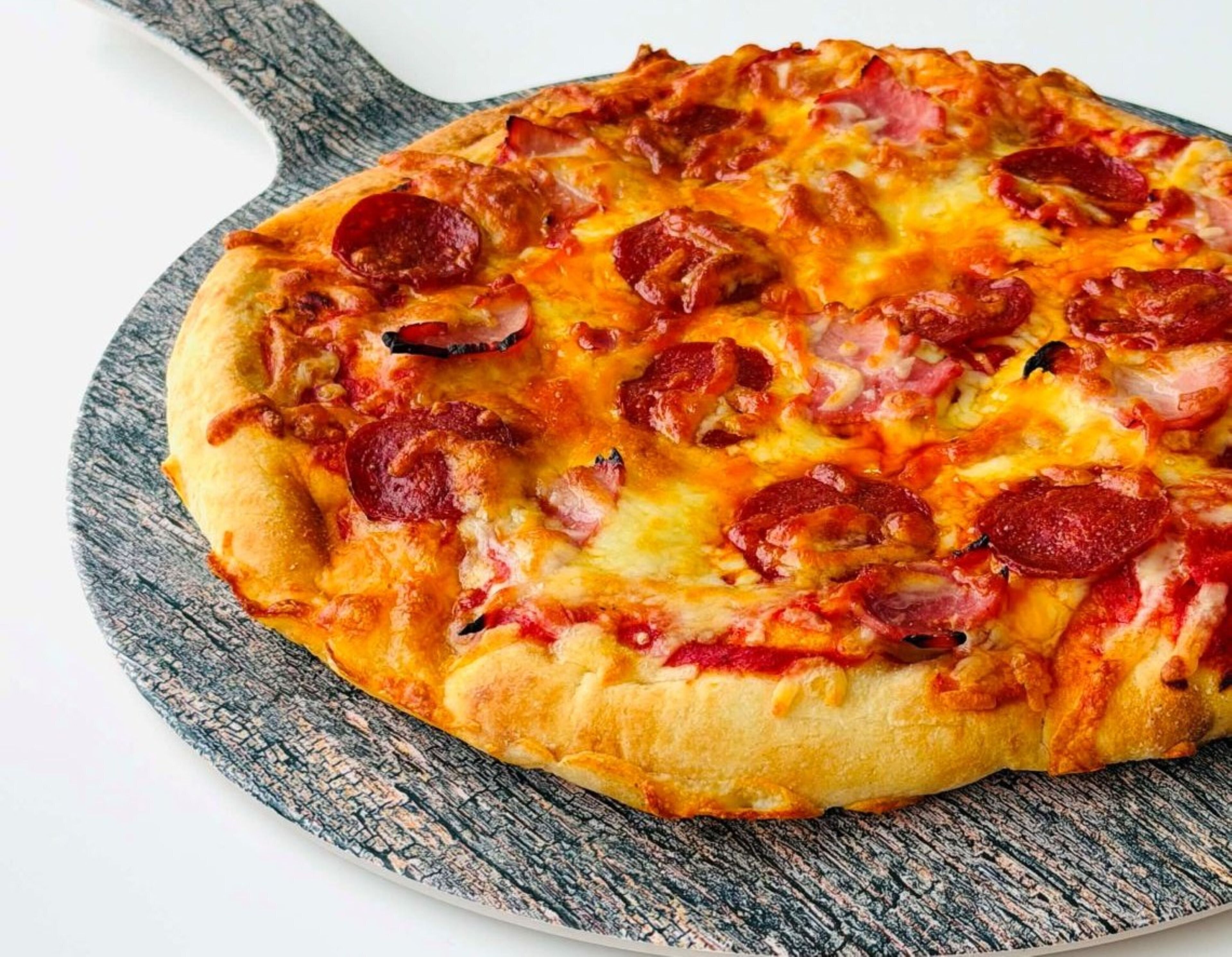 A pizza with pepperoni and ham toppings on a round wooden board.