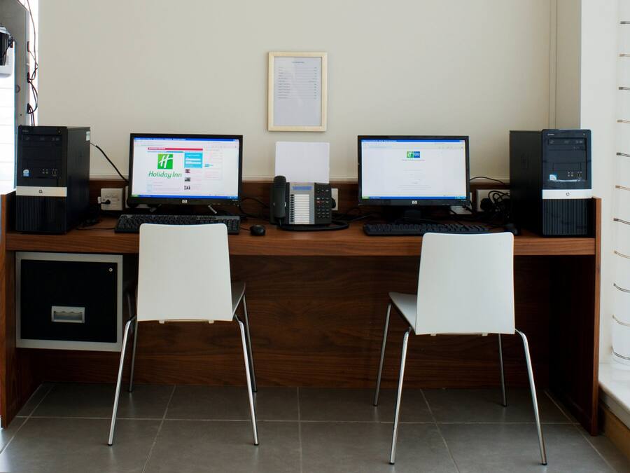 A workspace with two desks, each with a computer monitor, keyboard, and mouse. There are two chairs, a telephone, and a small cabinet.