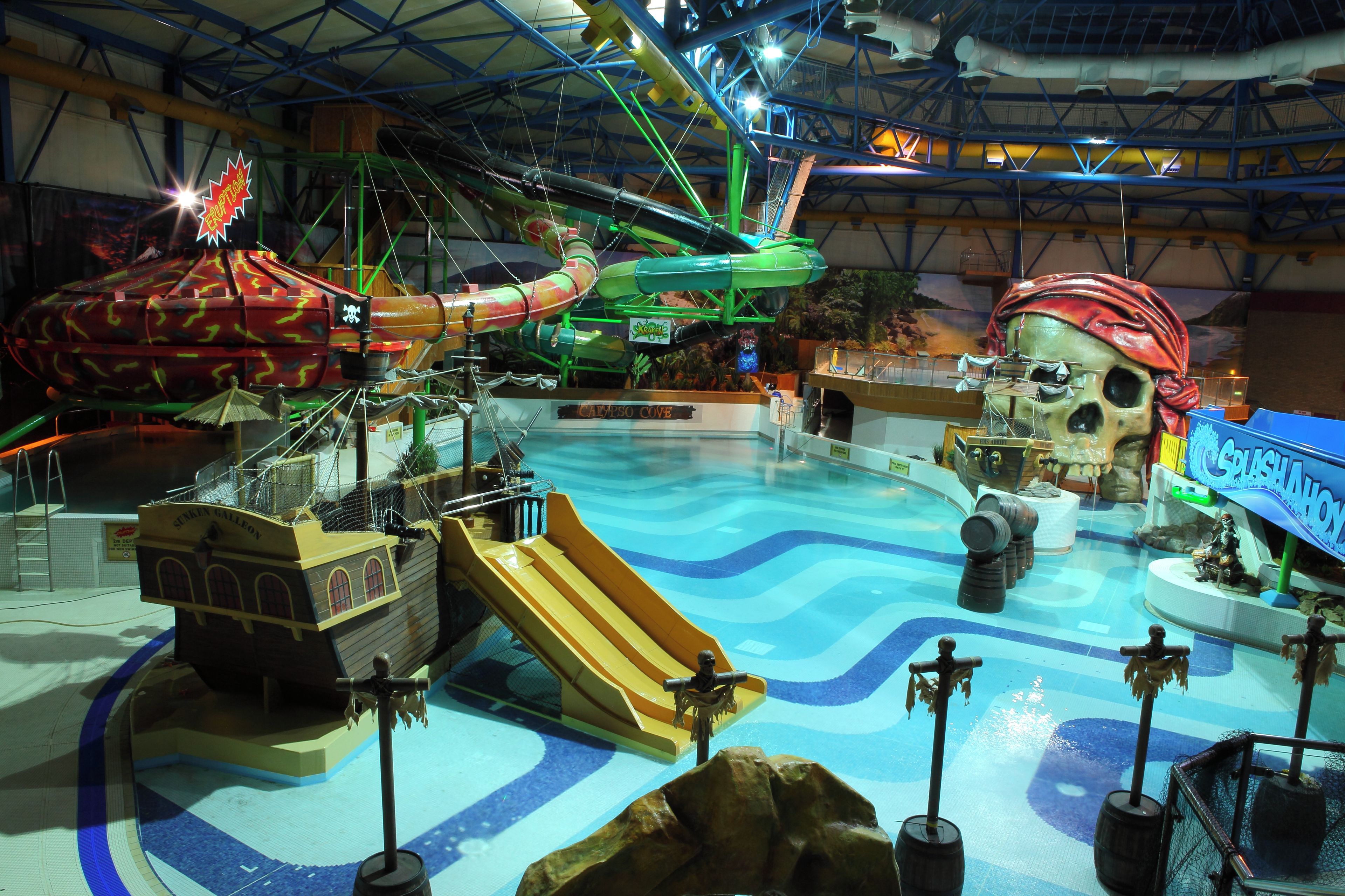 Un parque acuático interior con piscina de olas, toboganes y una zona temática pirata.