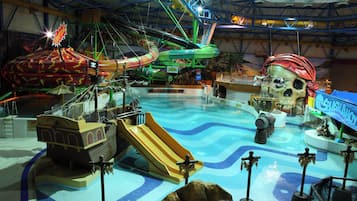 Un parque acuático interior con piscina de olas, toboganes y una zona temática pirata.
