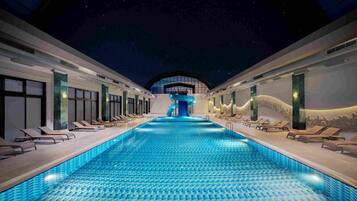 A swimming pool with a water slide, lounge chairs, and a night sky view.