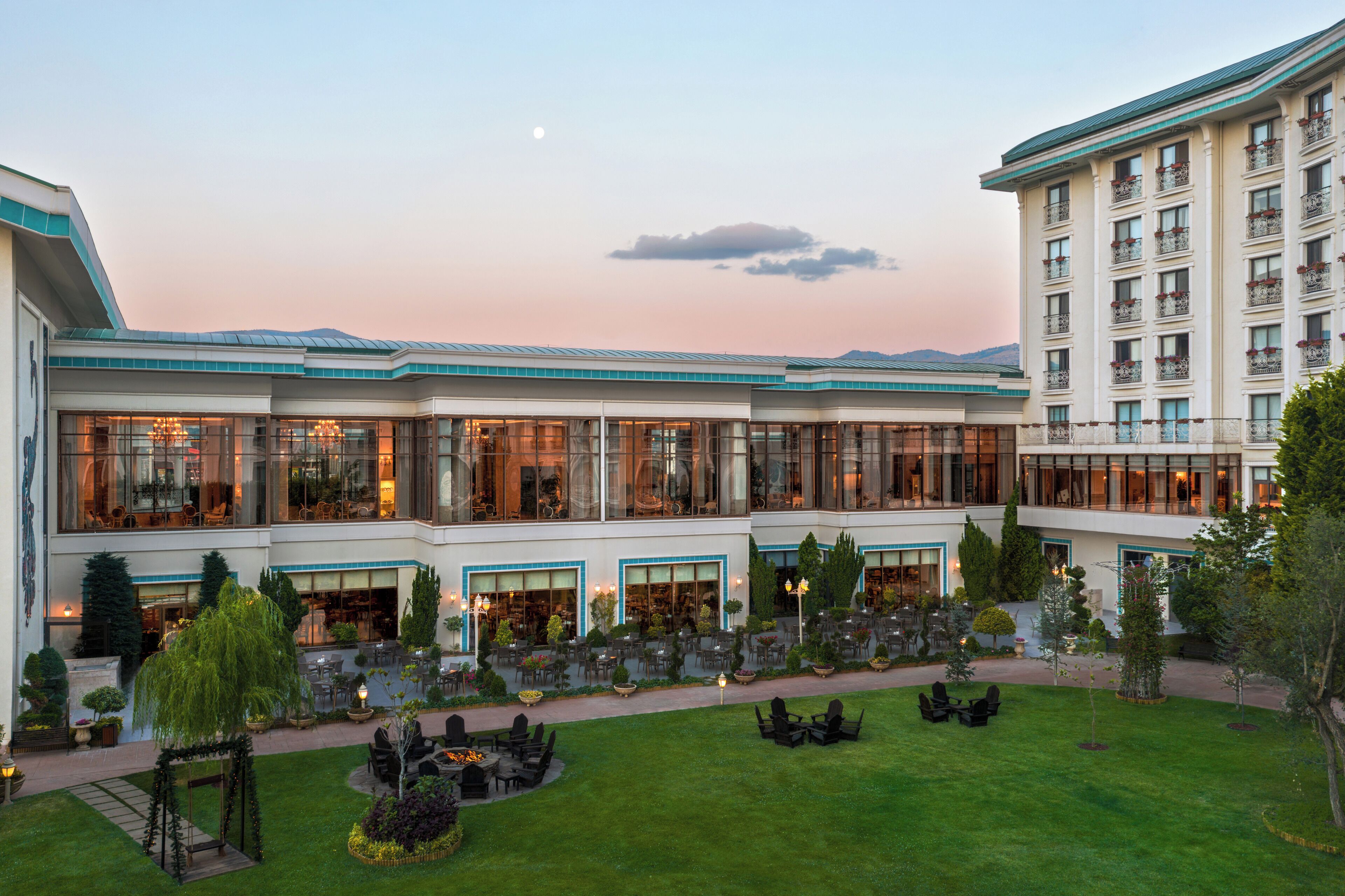Un hotel con varias plantas, amplias ventanas y un patio con mobiliario de exterior.